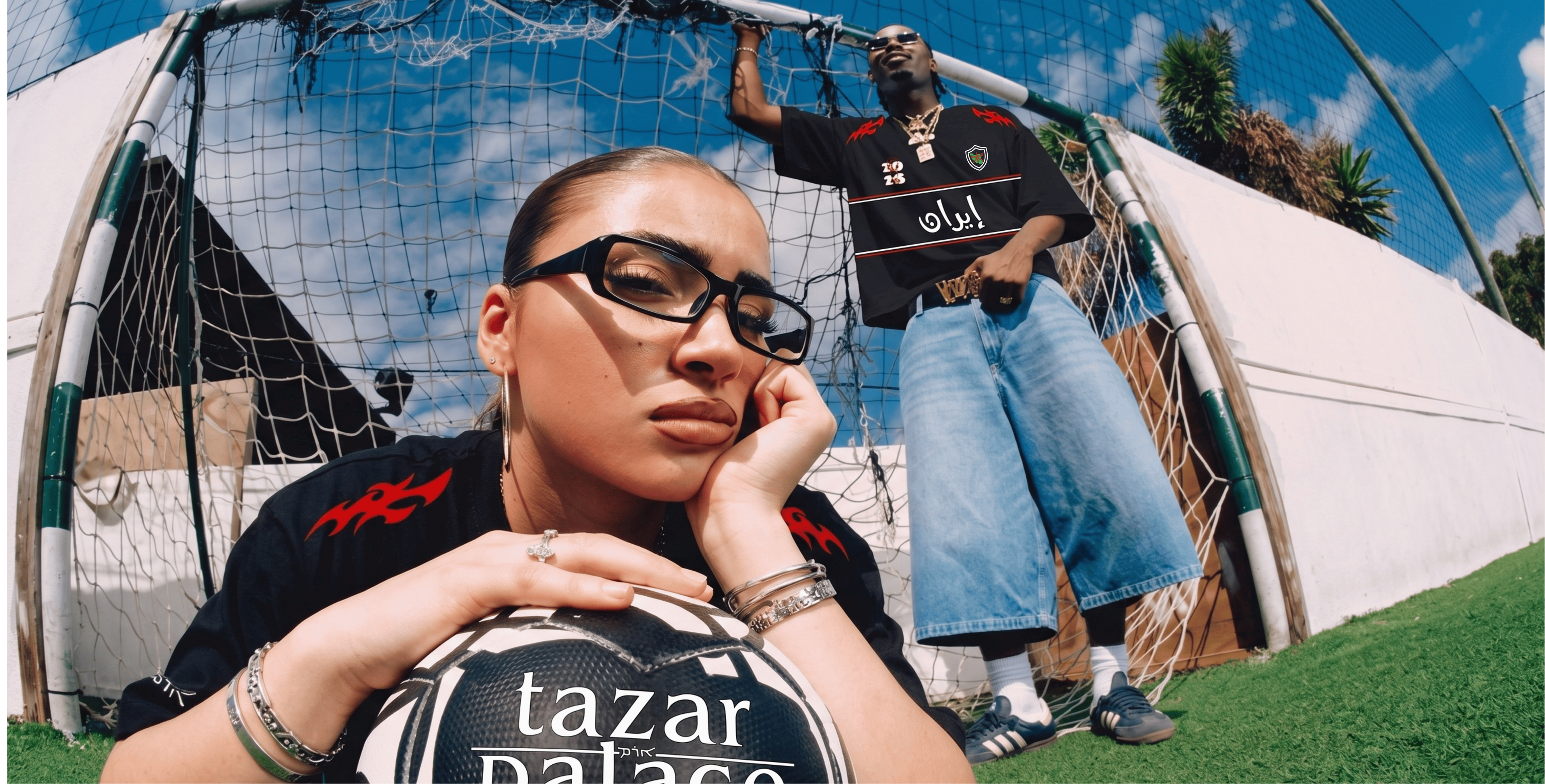 Two people in casual clothing with 'tazar palace' branding in a sports field setting.